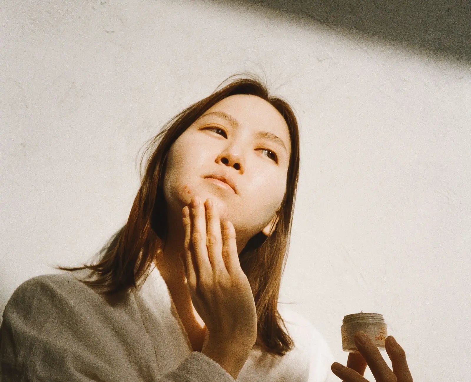 Woman smoothing moisturizer onto her cheek in soft morning light